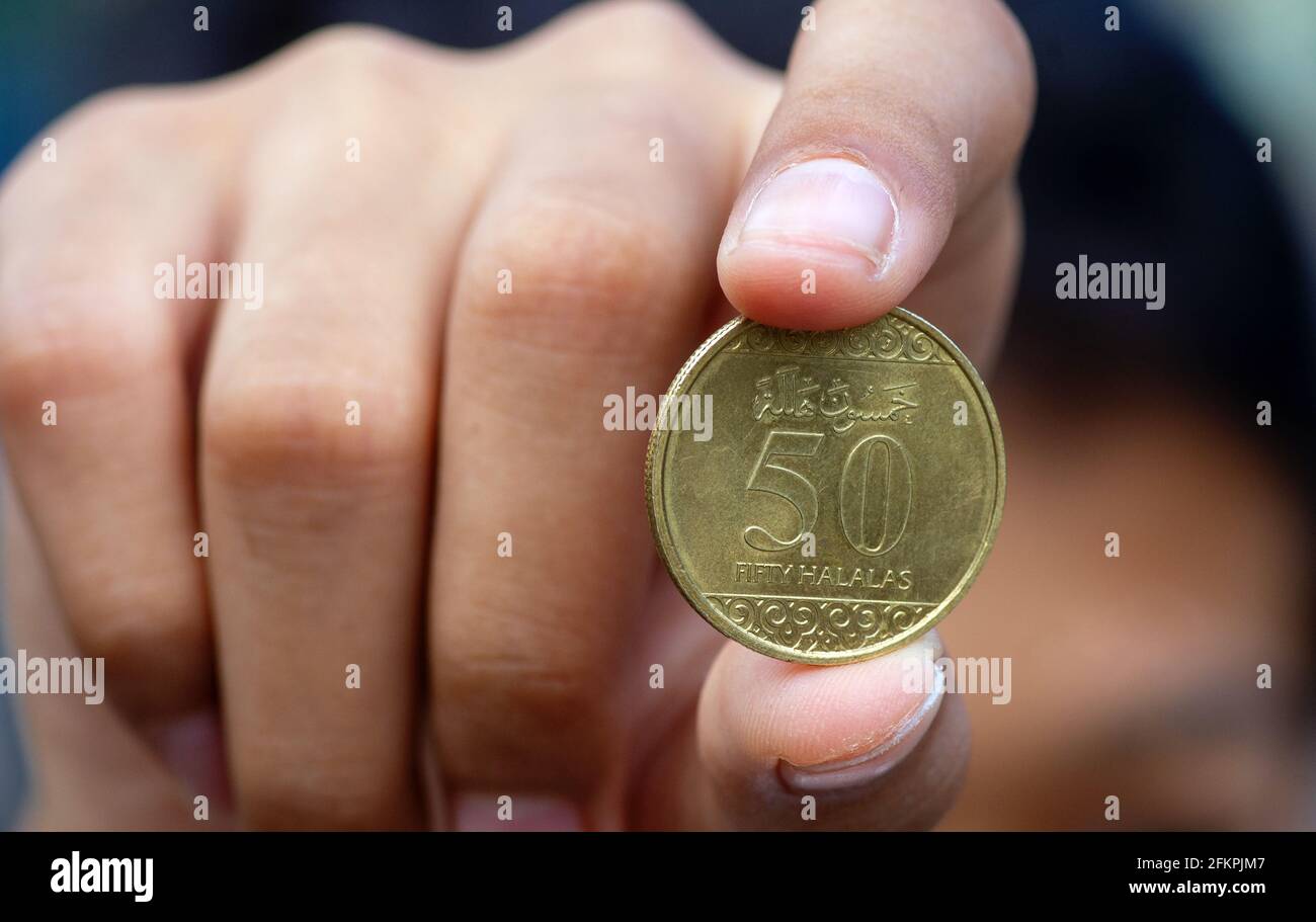 Asiatische Kinderhand mit einer Fifty Halalas Riyal-Münze, Saudi-Arabien-Geld, ausgewählter Fokus Stockfoto