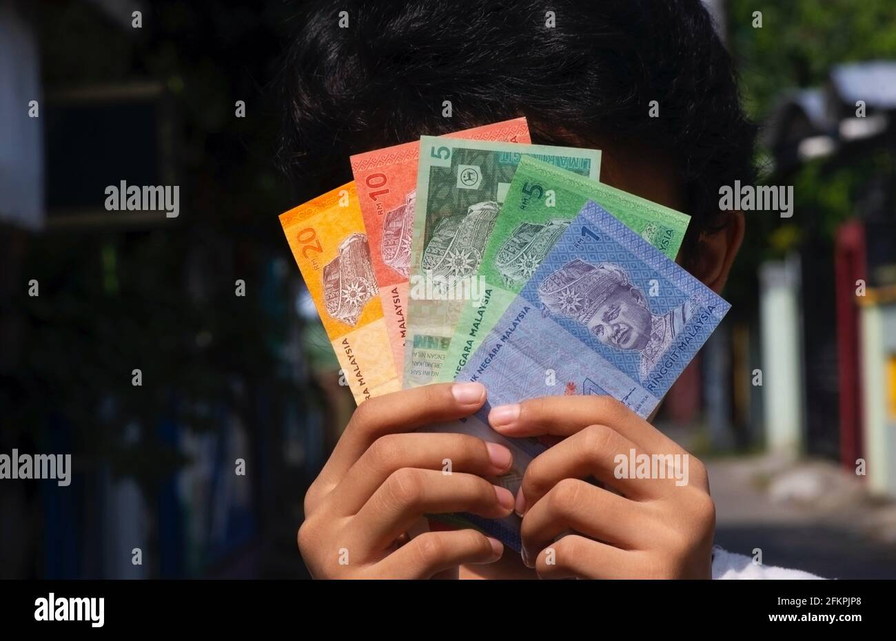 Asiatisches Kind hält Ringgit Malaysia Geld vor seinem Gesicht, ausgewählter Fokus. Konzept von Gehalt und Inflation Stockfoto