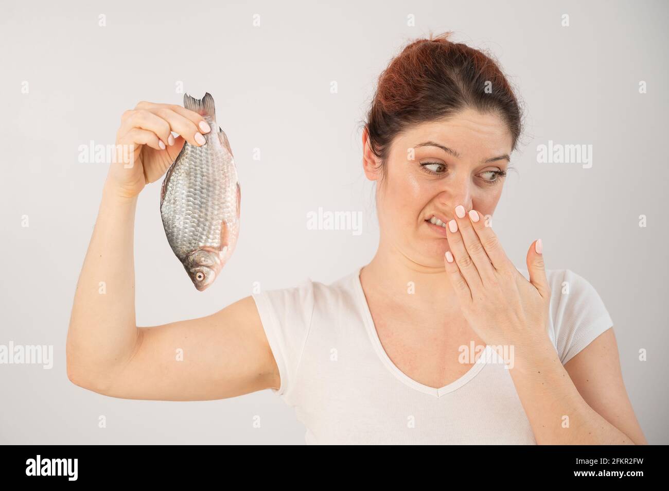 Kaukasische Frau widersetzt sich dem widerlichen Geruch von Fisch. Eine Metapher für die Gesundheit und Intimhygiene von Frauen. Stockfoto