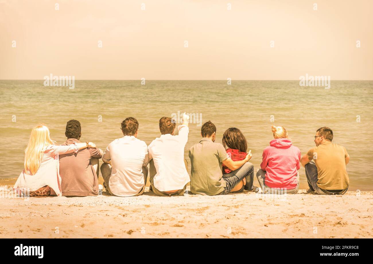 Gruppe internationaler multirassischer Freunde, die am Strand sitzen und sich unterhalten Miteinander und das Meer betrachten Stockfoto