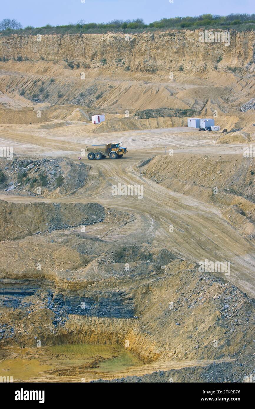 Ein großer artikulierter LKW, der von den Klippen in einem riesigen Steinbruch in den Schatten gestellt wird. England, Großbritannien. Stockfoto