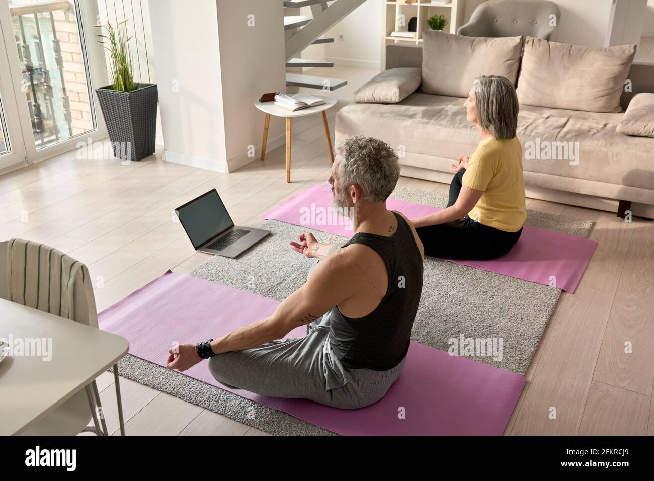 Seniorehepaar meditiert dabei virtuelle Yoga-Posen beobachten Online-Kurs zu Hause. Stockfoto