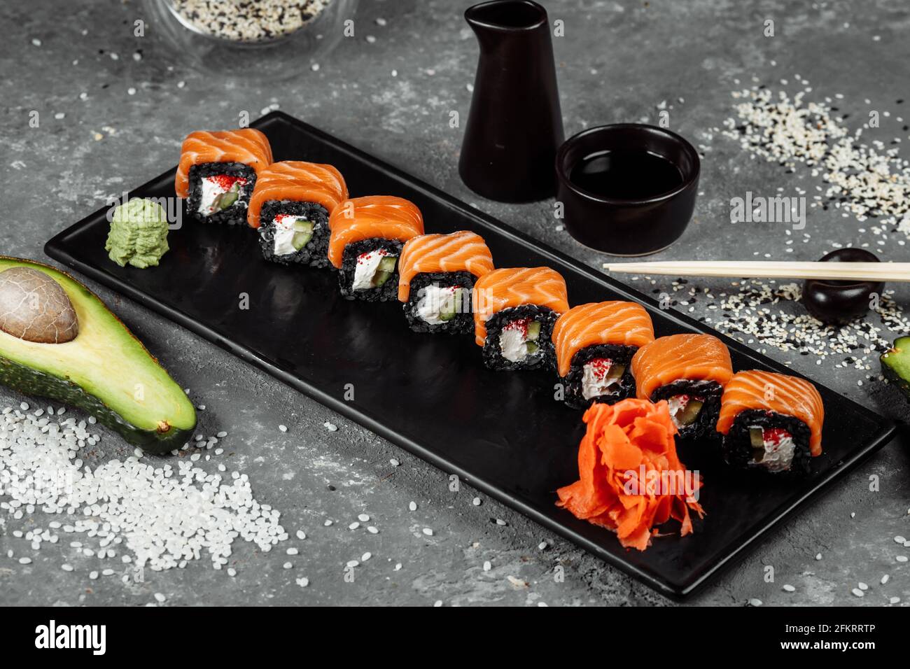 Eine Reihe von Sushi-Rollen Philadelphia mit rotem Fisch, Frischkäse und schwarzem Rise liegt auf einem Teller Boot. Sushi rollt auf grauem Hintergrund Stockfoto