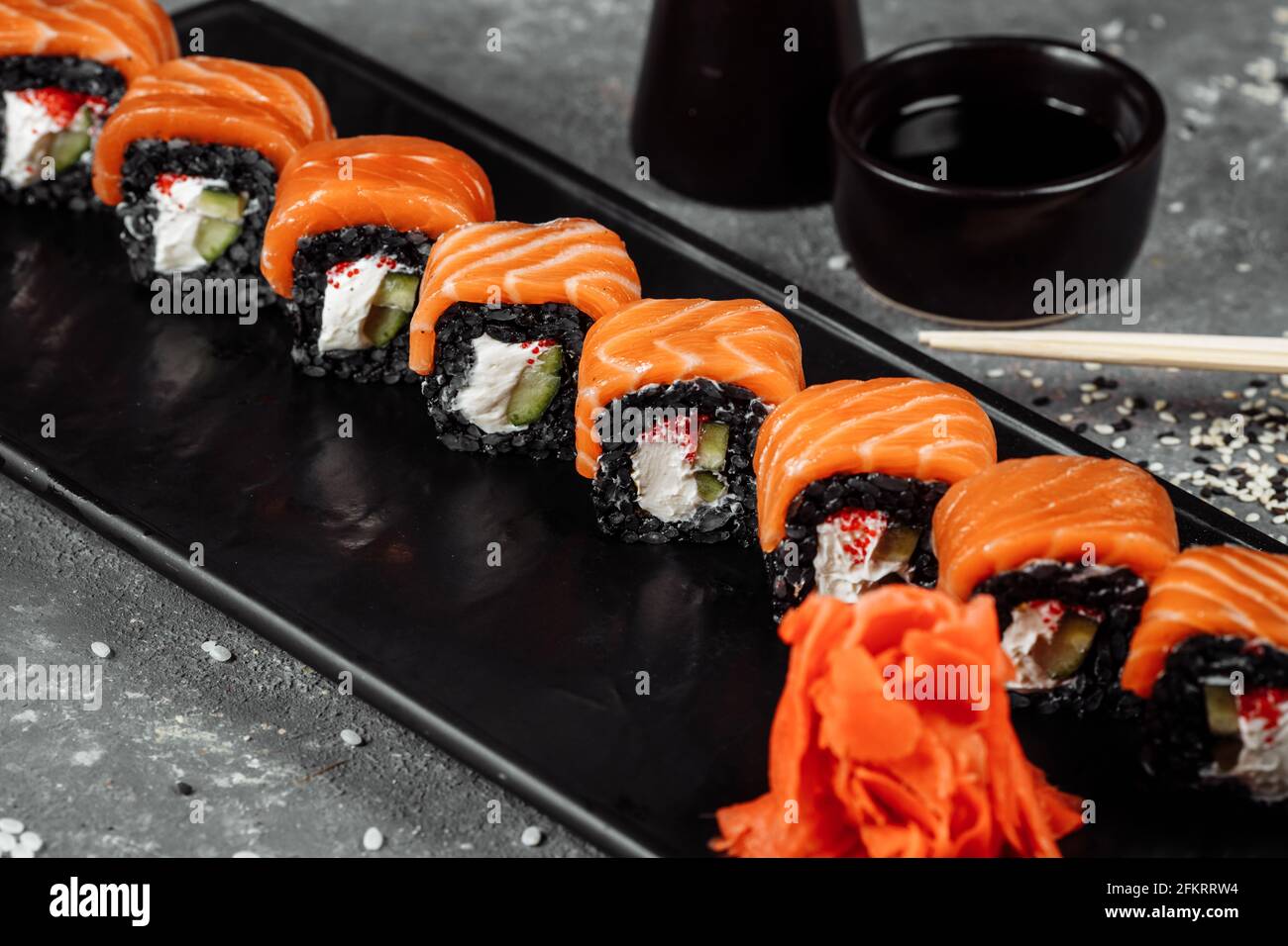 Eine Reihe von Sushi-Rollen Philadelphia mit rotem Fisch, Frischkäse und schwarzem Rise liegt auf einem Teller Boot. Sushi rollt auf grauem Hintergrund Stockfoto