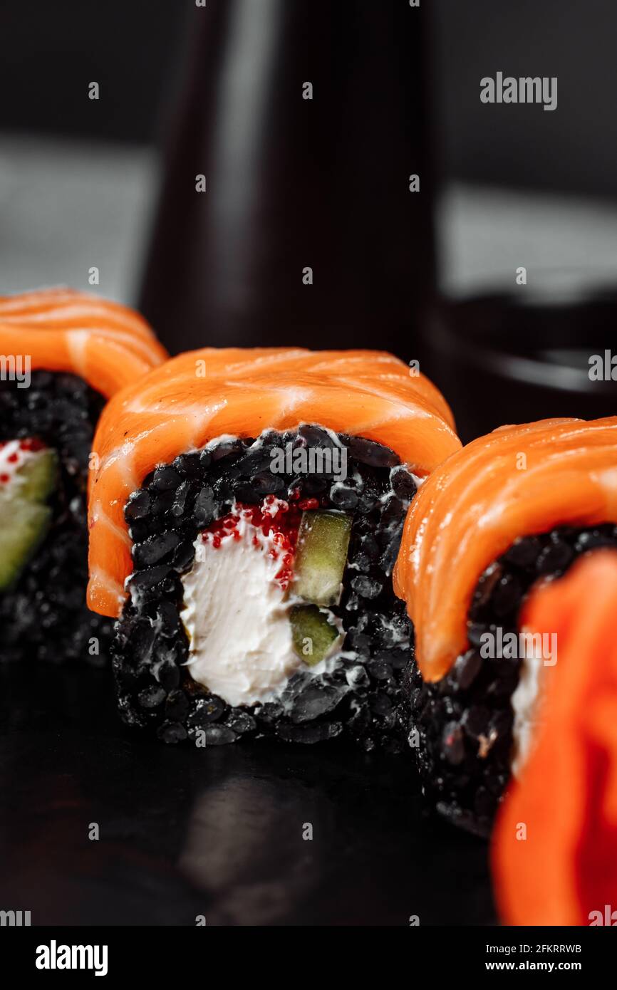 Eine Reihe von Sushi-Rollen Philadelphia mit rotem Fisch, Frischkäse und schwarzem Rise liegt auf einem Teller Boot. Sushi rollt auf grauem Hintergrund Stockfoto