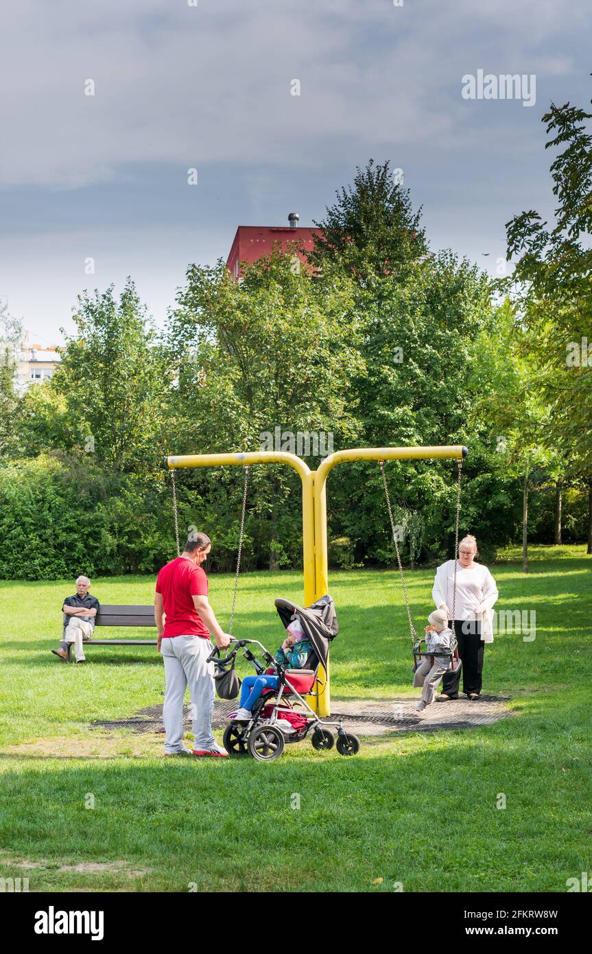 POZNAN, POLEN - 11. Sep 2017: Mann und Frau mit zwei Kindern, darunter ein Kind, das in einem Buggy durch eine Schaukel auf einem Spielplatz behindert ist. Stockfoto
