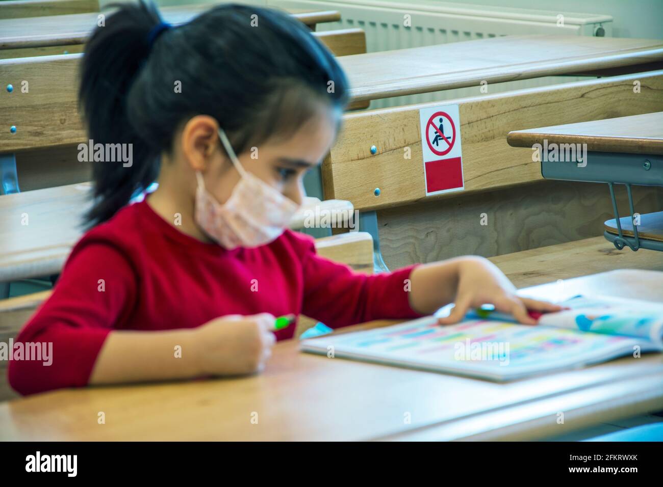 Fokussiertes Bild auf nicht hier sitzen Label hinter Mädchen Lernen im leeren Klassenzimmer mit Schutzmaske Stockfoto