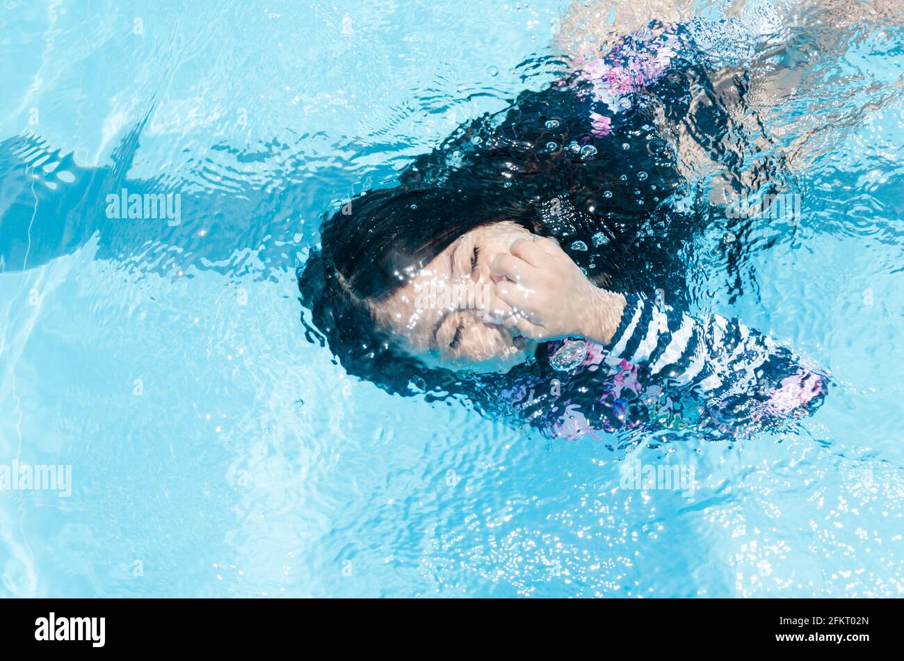 Das Mädchen im Pool schwimmt unter Wasser und lächelt und hält ihre Nase. Stockfoto