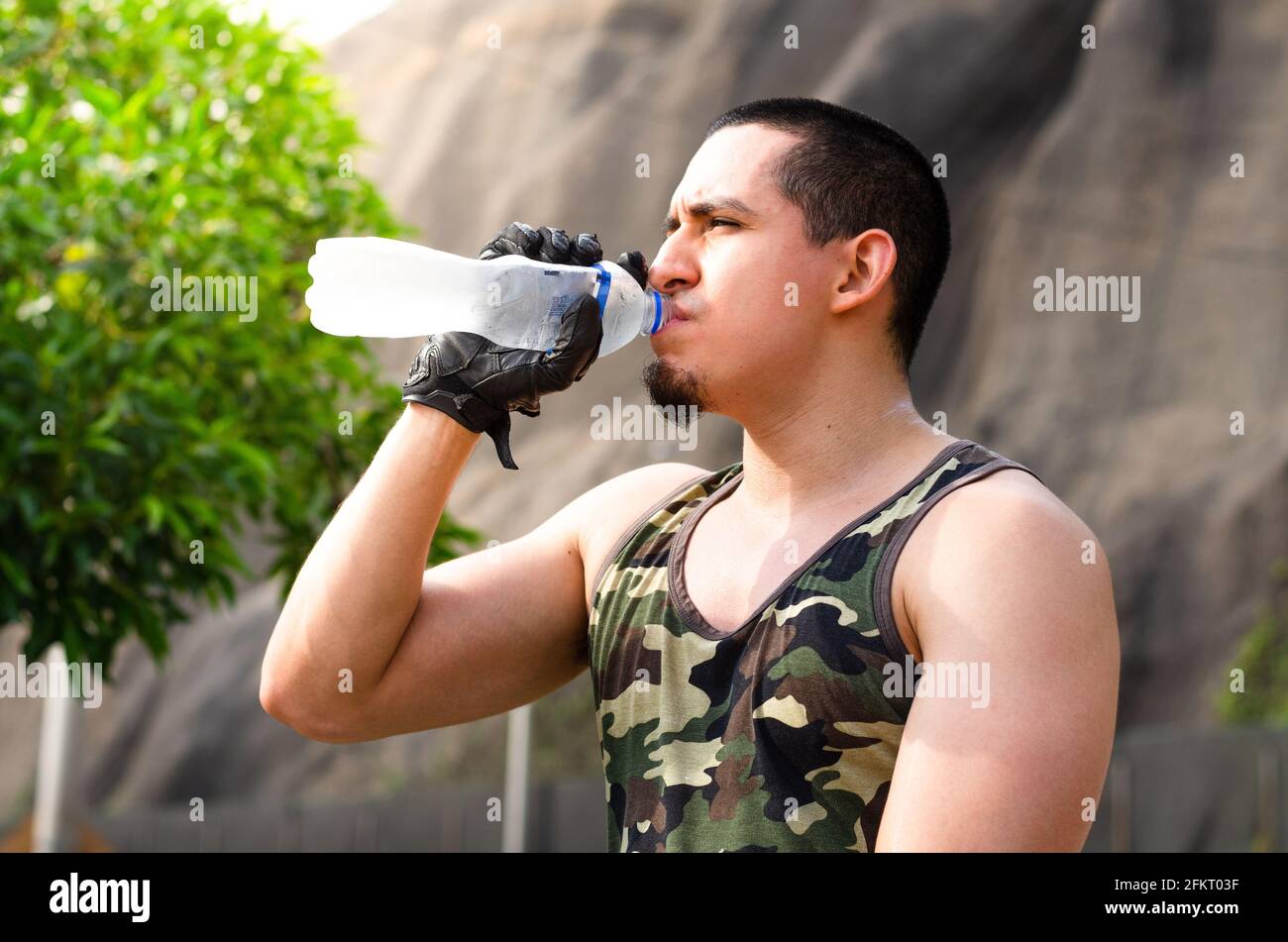 Erschöpfter junger Athlet, der während einer Laufstrecke frisches Wasser trinkt, um sich abzukühlen. Stockfoto