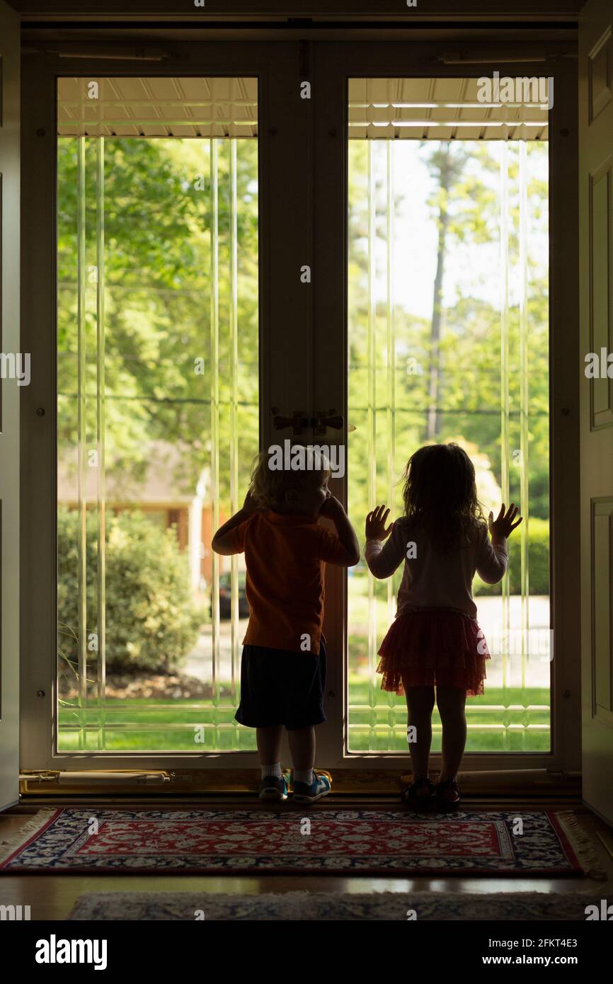Männlichen und weiblichen Kleinkind Freunde Silhouette durch die Terrassentür Stockfoto