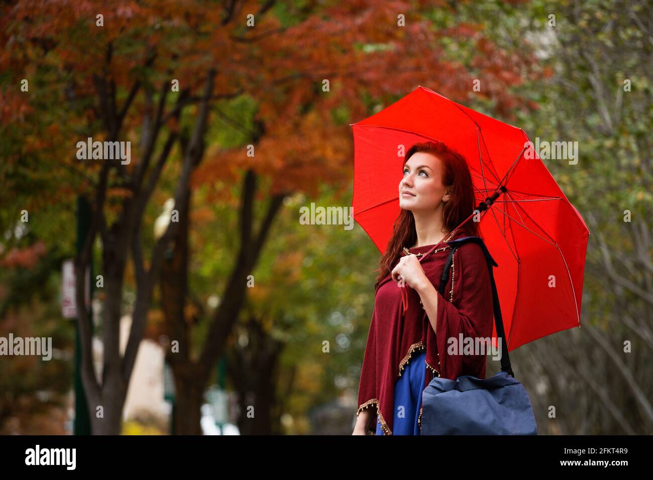 Junge Frau mit roten Haaren, mit roten Regenschirm Stockfoto