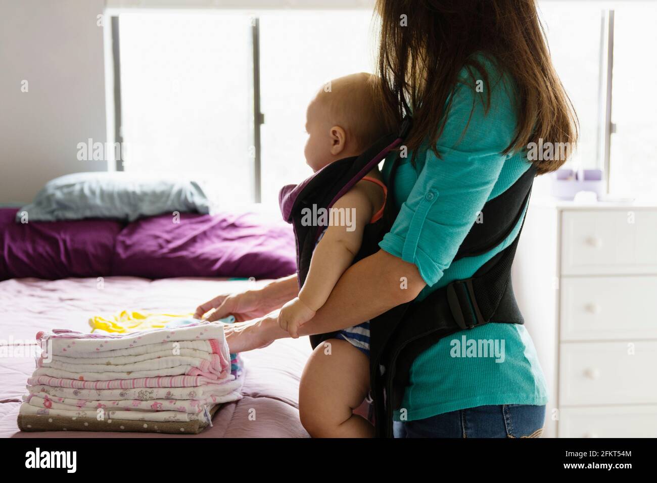 Mitte Erwachsene Frau tun Hausarbeit mit Tochter im Tragetuch Stockfoto