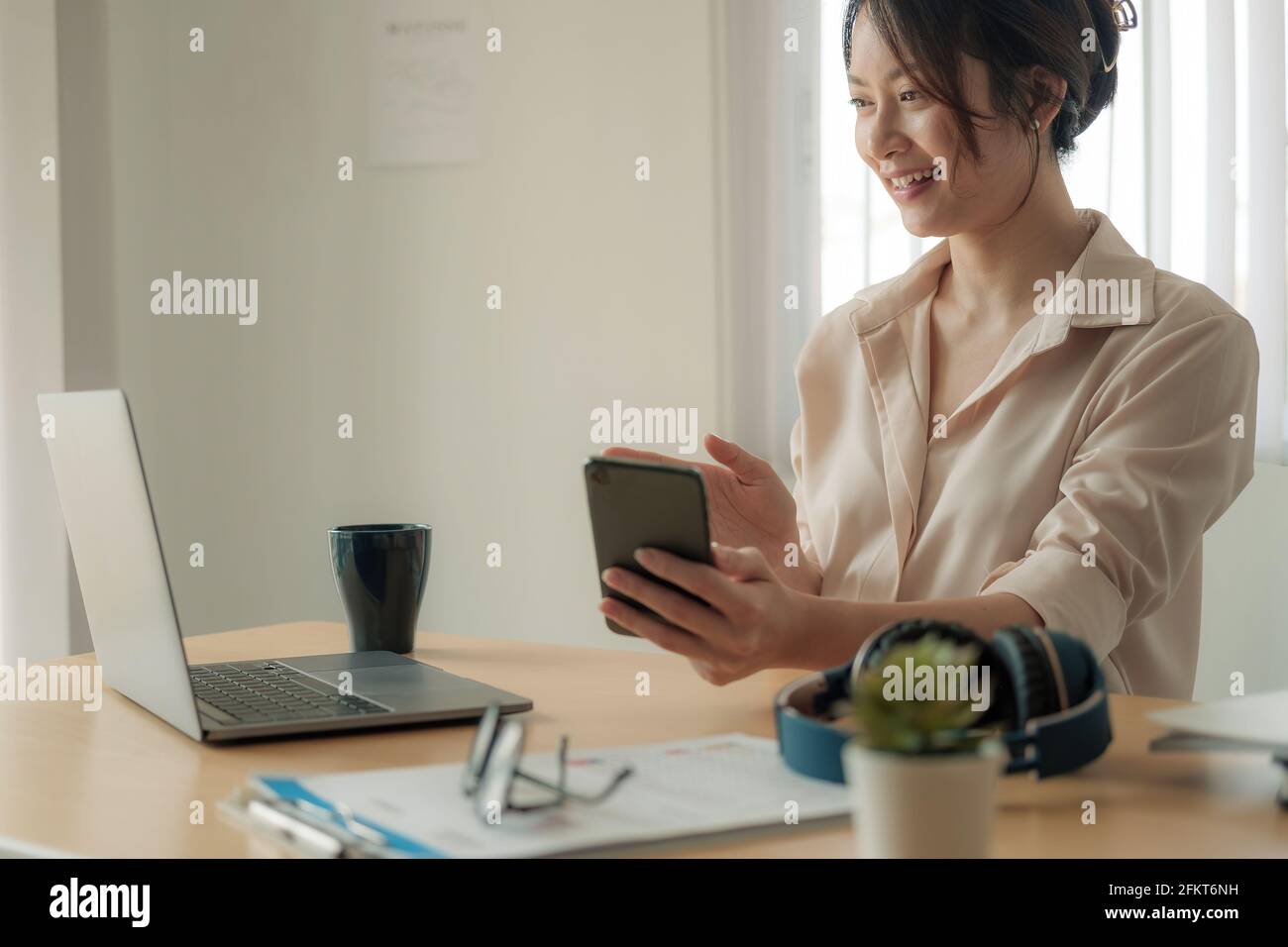 Attraktive asiatische Frau mit Videoanruf über Laptop und Mobiltelefon im Heimbüro, Beratung, Webinar, Nachhilfe im Internet, Telearbeit Stockfoto