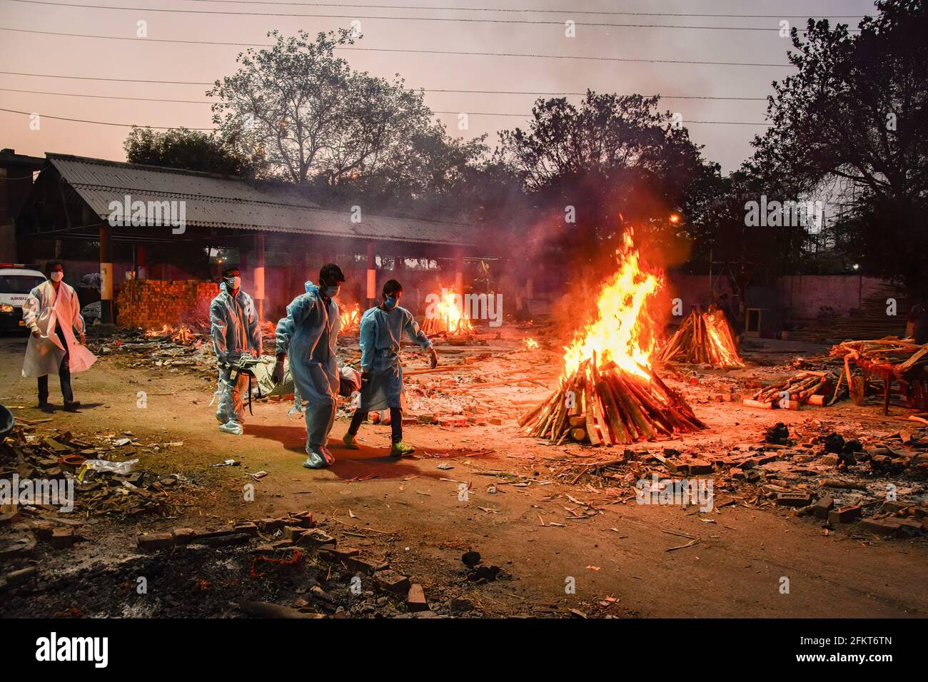 Neu-Delhi, Indien. Mai 2021. (ANMERKUNG DER REDAKTION: Bild zeigt den Tod) Arbeiter tragen den Körper einer Person, die an der Coronavirus-Krankheit Covid-19 gestorben ist, während andere Scheiterhaufen während einer Massenverbrennung in einem Krematorium verbrannt werden. Indien hat seit Beginn des Ausbruchs insgesamt 19.9 Millionen Fälle und 219,000 Todesfälle verzeichnet. Kredit: SOPA Images Limited/Alamy Live Nachrichten Stockfoto