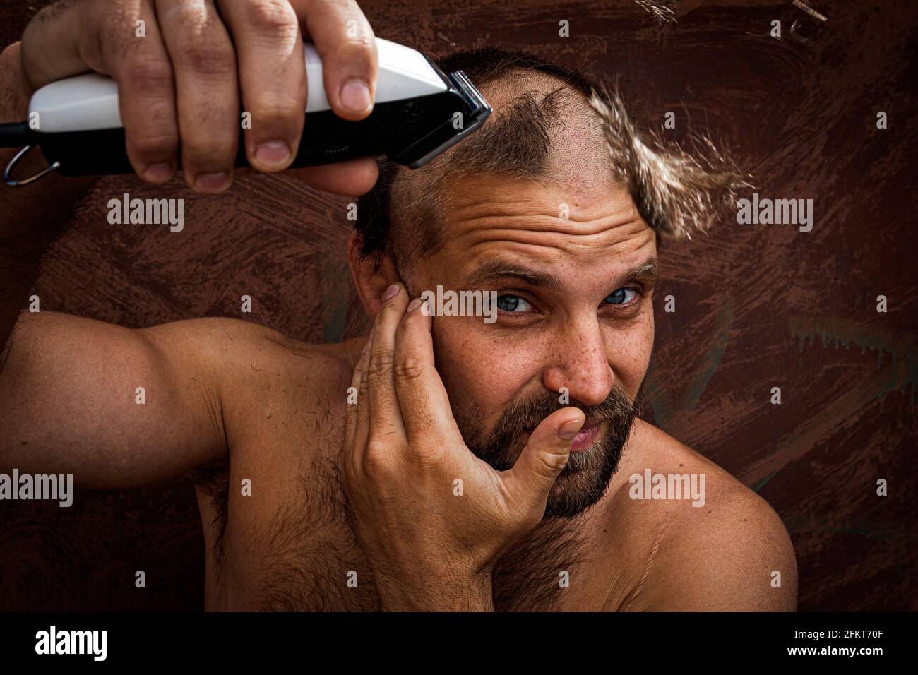 Kaukasischer Mann, der versucht, seinen Kopf mit einem elektrischen  Rasiermesser zu rasieren. Ein brutaler Glatze hält einen Rasierer in der  Hand und rasiert Stoppeln auf einem metallischen Hintergrund  Stockfotografie - Alamy