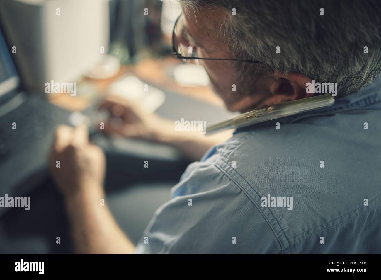Ein älterer Mann, der vor einem Schreibtisch sitzt Ein Laptop-Computer Stockfoto