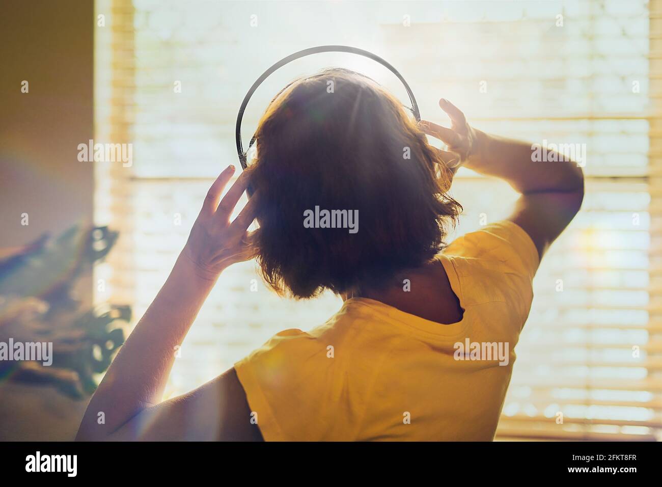Eine Frau mit Kopfhörer oder Headset auf dem Kopf mit dem Fenster und Sonnenlicht auf dem Hintergrund. Stockfoto