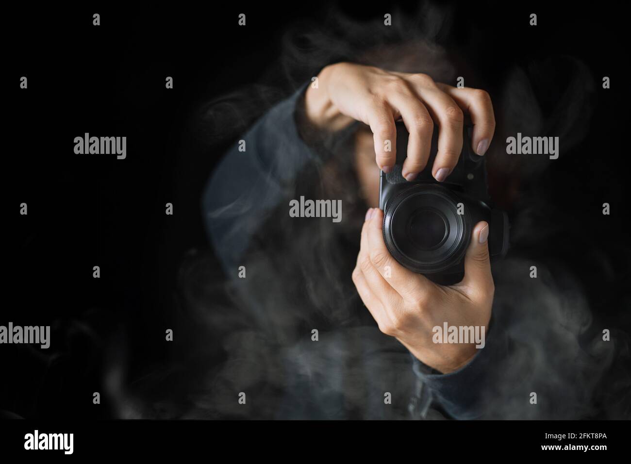 Die Hände der Frau hielten die Fotokamera. Nahaufnahme. Eine Person in schwarzem Hoodie und Rauch um Stockfoto