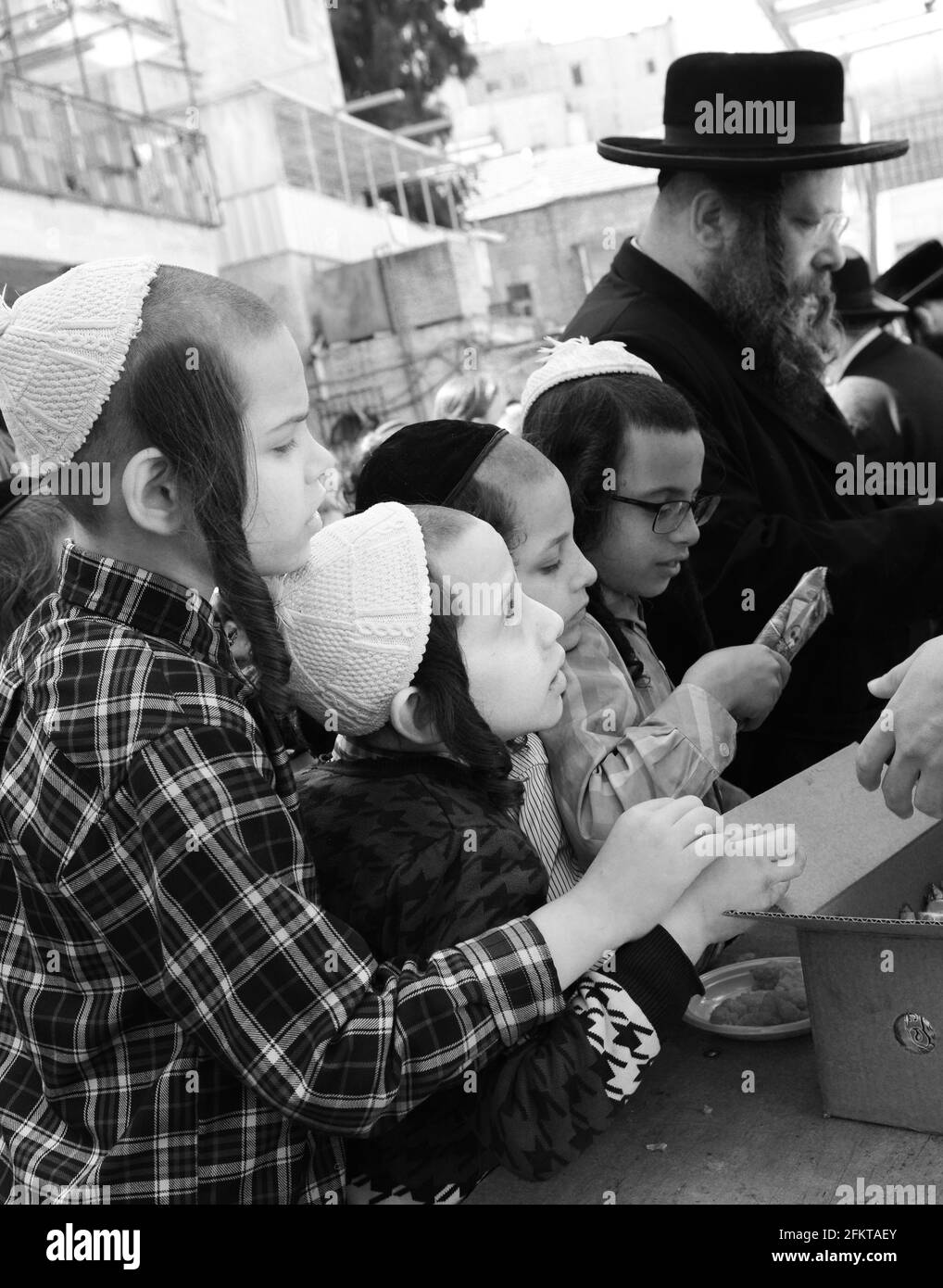 Jüdisch-orthodoxe Kinder warten in der Schlange auf Essen und Süßigkeiten, die von einem rechtschaffenen jüdischen Mann während der Passahvorbereitungen in Mea She'arim Jerusalem serviert werden. Stockfoto