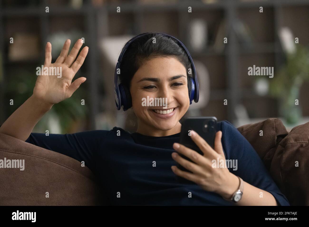 Nahaufnahme einer indischen Frau in Kopfhörern, die mit der Hand winkt, mit dem Smartphone Stockfoto