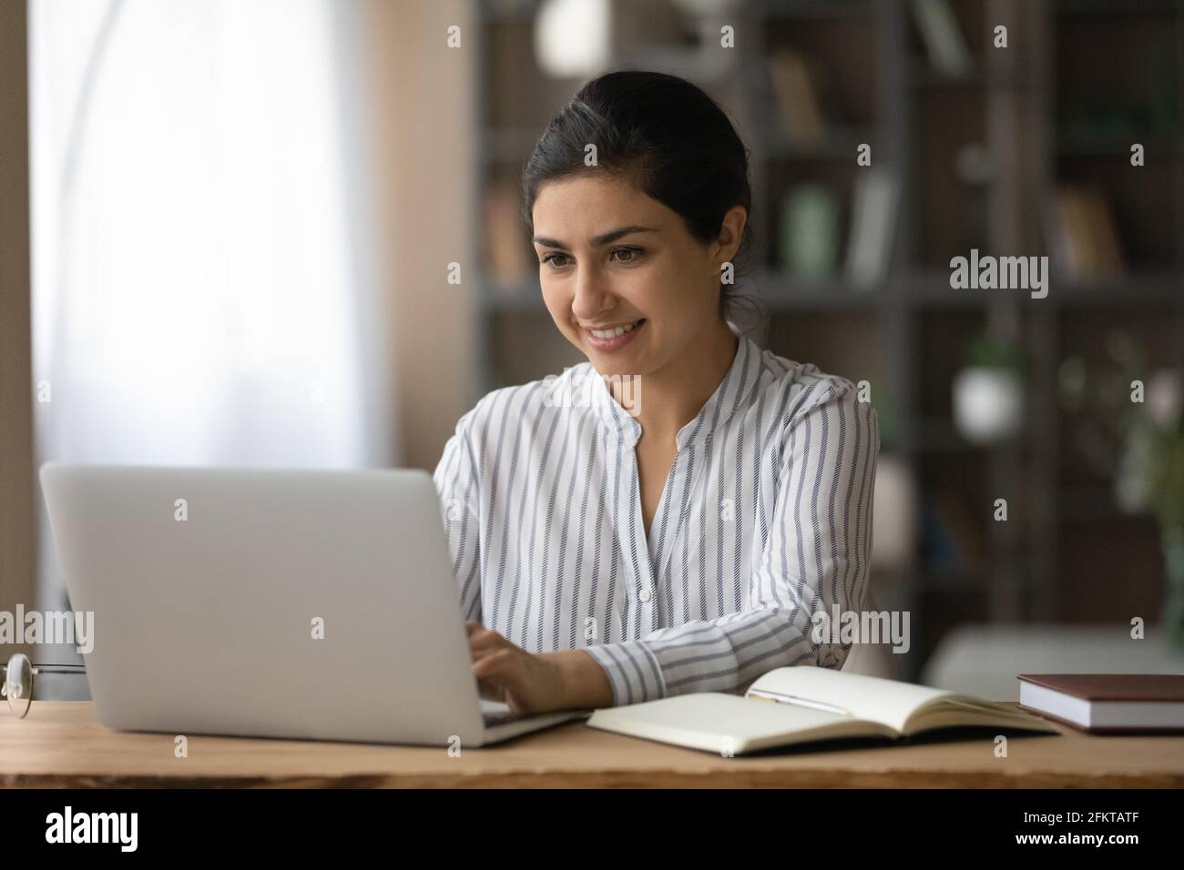 Lächelnde Inderin mit Laptop, online zu Hause studieren Stockfoto