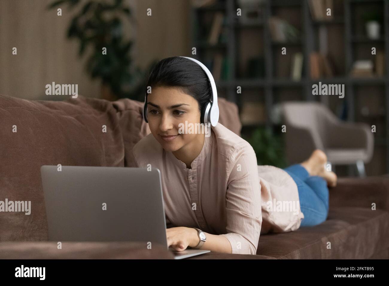 Nahaufnahme einer indischen Frau in Kopfhörern mit Laptop auf der Couch Stockfoto