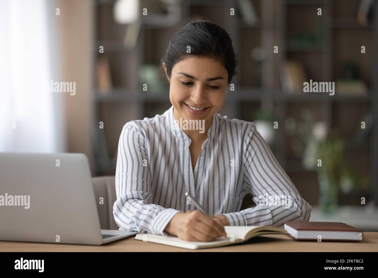 Nahaufnahme lächelnde Inderin, die sich Notizen macht, zu Hause studiert Stockfoto