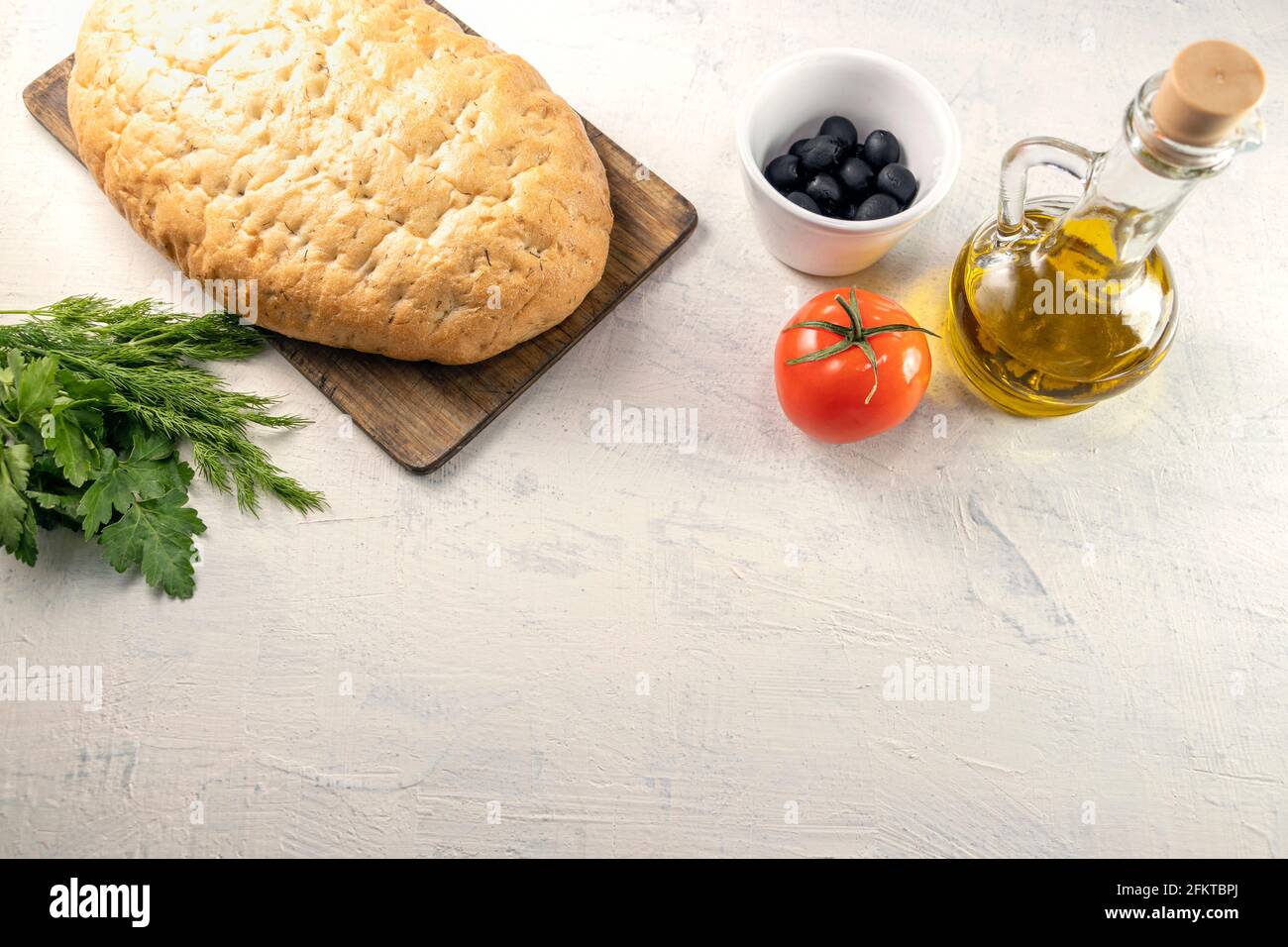 Serviert aus italienischem Focaccia.frisches, leckeres Brot mit aromatischen Kräutern auf Holzbrett neben schwarzen Oliven, Tomaten, Petersilie und Olivenöl auf weißer Textur Stockfoto