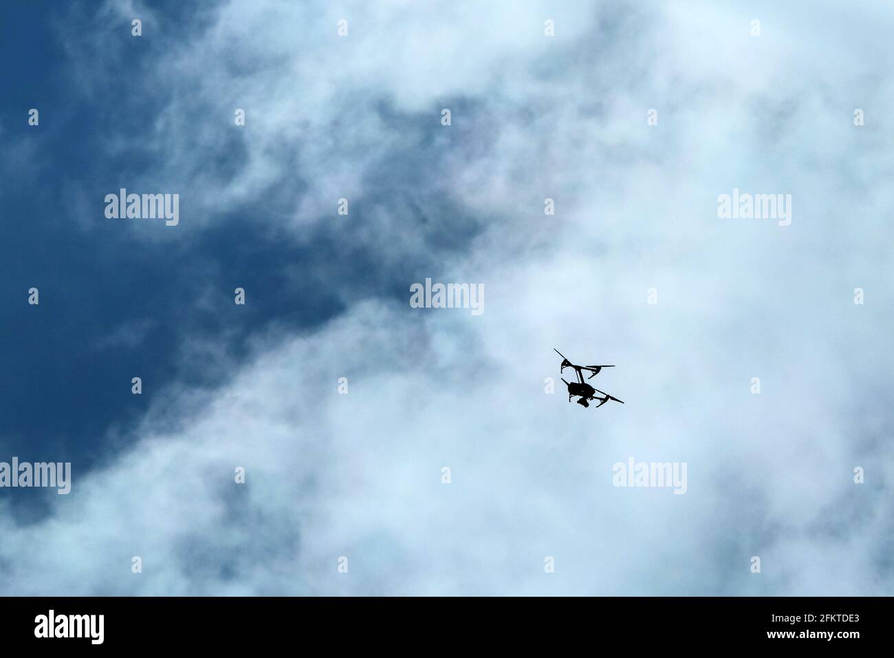 Die kleine Drohne, die hoch fliegt, ist gegen den bewölkten Himmel abgebildet. Nur die Silhouette ist sichtbar. Stockfoto