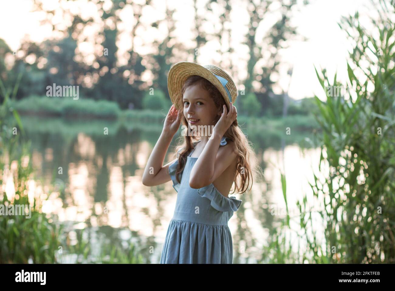 Ein Mädchen in blauem Kleid und Strohhut steht auf Das Ufer des Sees Stockfoto