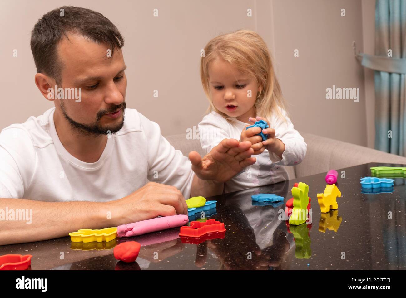 Vater und Kind spielen zu Hause zusammen und machen Tiere aus buntem Spielteig Stockfoto