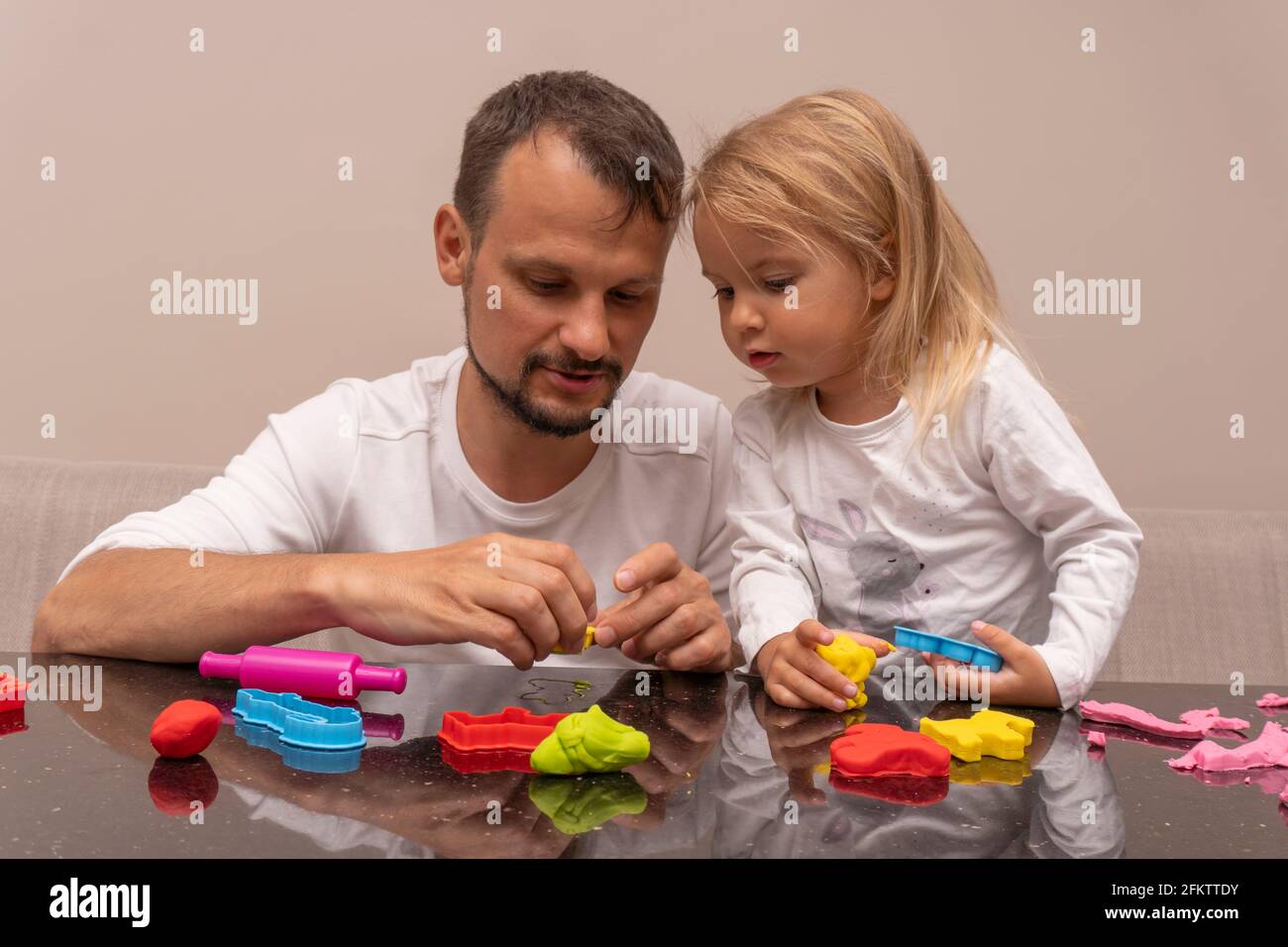 Der kaukasische Mann spielt mit seiner Tochter und macht bunte Tiere Spielteig Stockfoto