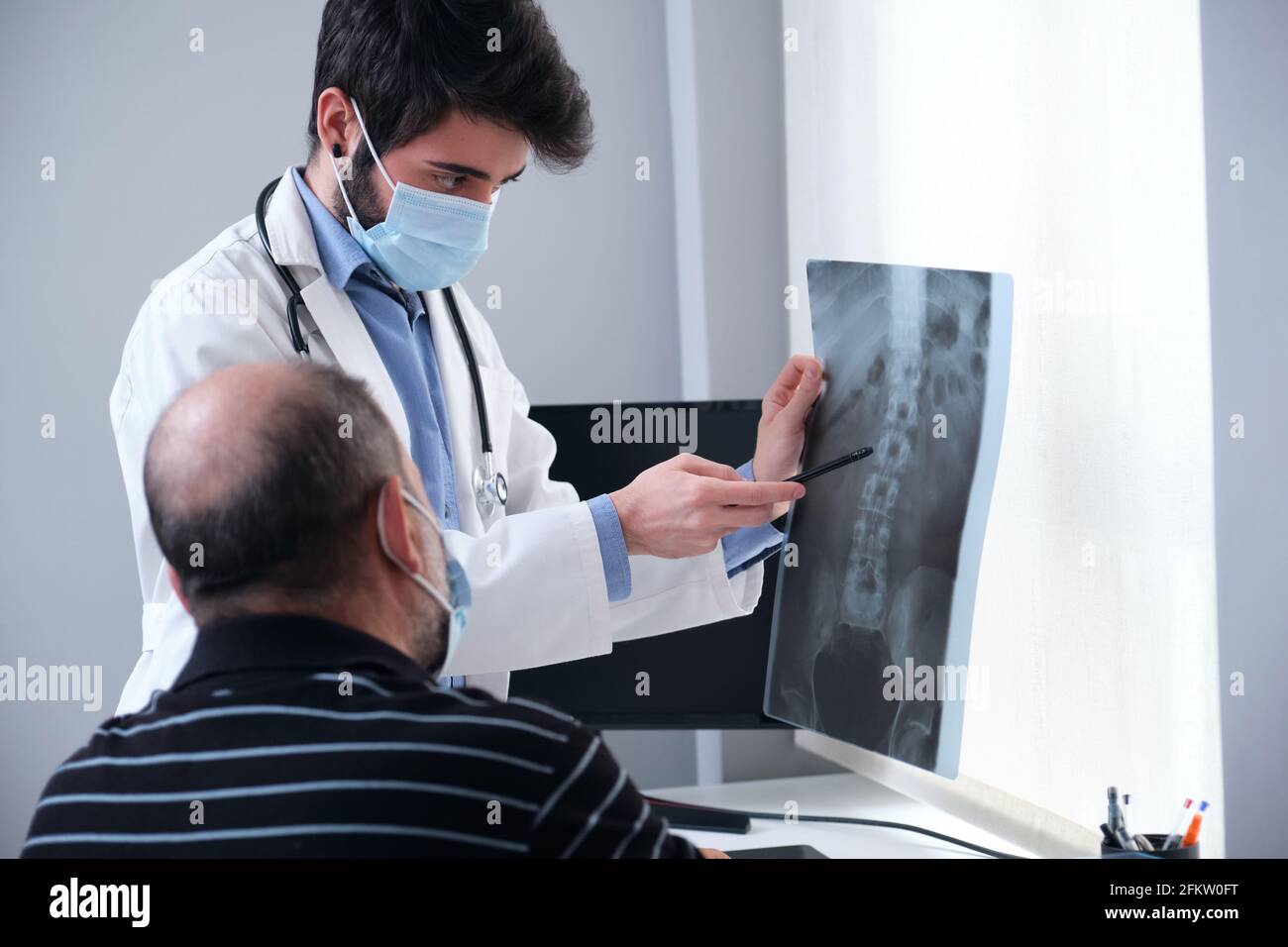 Junger Arzt, der die Röntgenaufnahme eines älteren Patienten untersucht. Radiographie einer Wirbelsäule, Wirbelsäule oder Wirbelsäule. Stockfoto