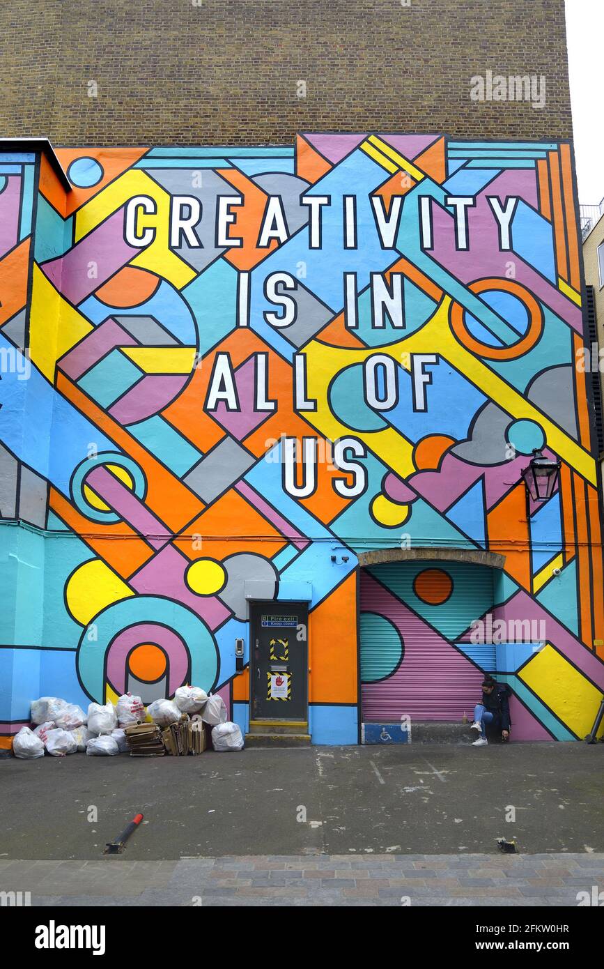 London, England, Großbritannien. London Graphic Center – Wandgemälde an der Fassade der Mercer Street. Frau, die auf der Stufe sitzt, und Müllsäcke Stockfoto London, England, Großbritannien. London Graphic Center – Wandgemälde an der Fassade der Mercer Street. Frau, die auf der Stufe sitzt, und Müllsäcke Stockfoto