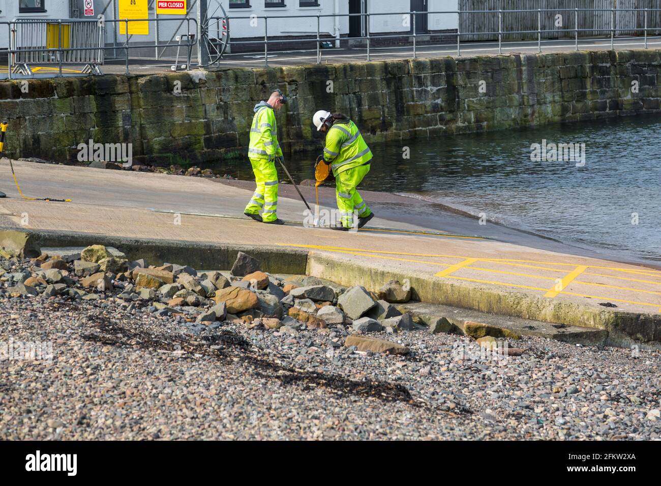 Zwei Arbeiter, die gelbe Linien auf einem Slipway malen, Schottland, Großbritannien Stockfoto