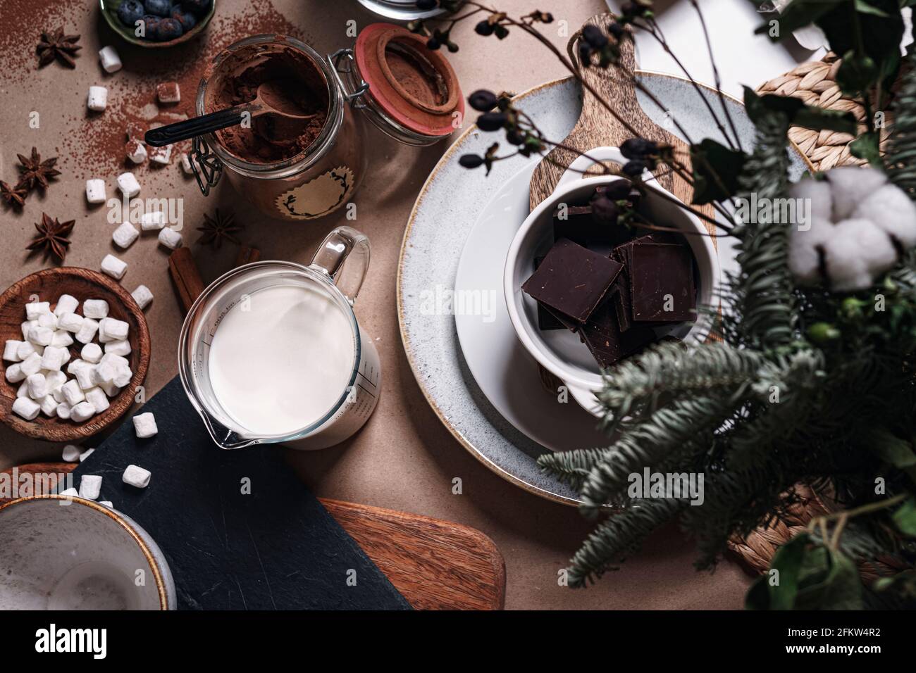 Zutaten zum Kochen heißer Schokolade, darunter Milch, Kakao, dunkle Schokolade, Gewürze, Salmler und Küchengeräte. Stockfoto