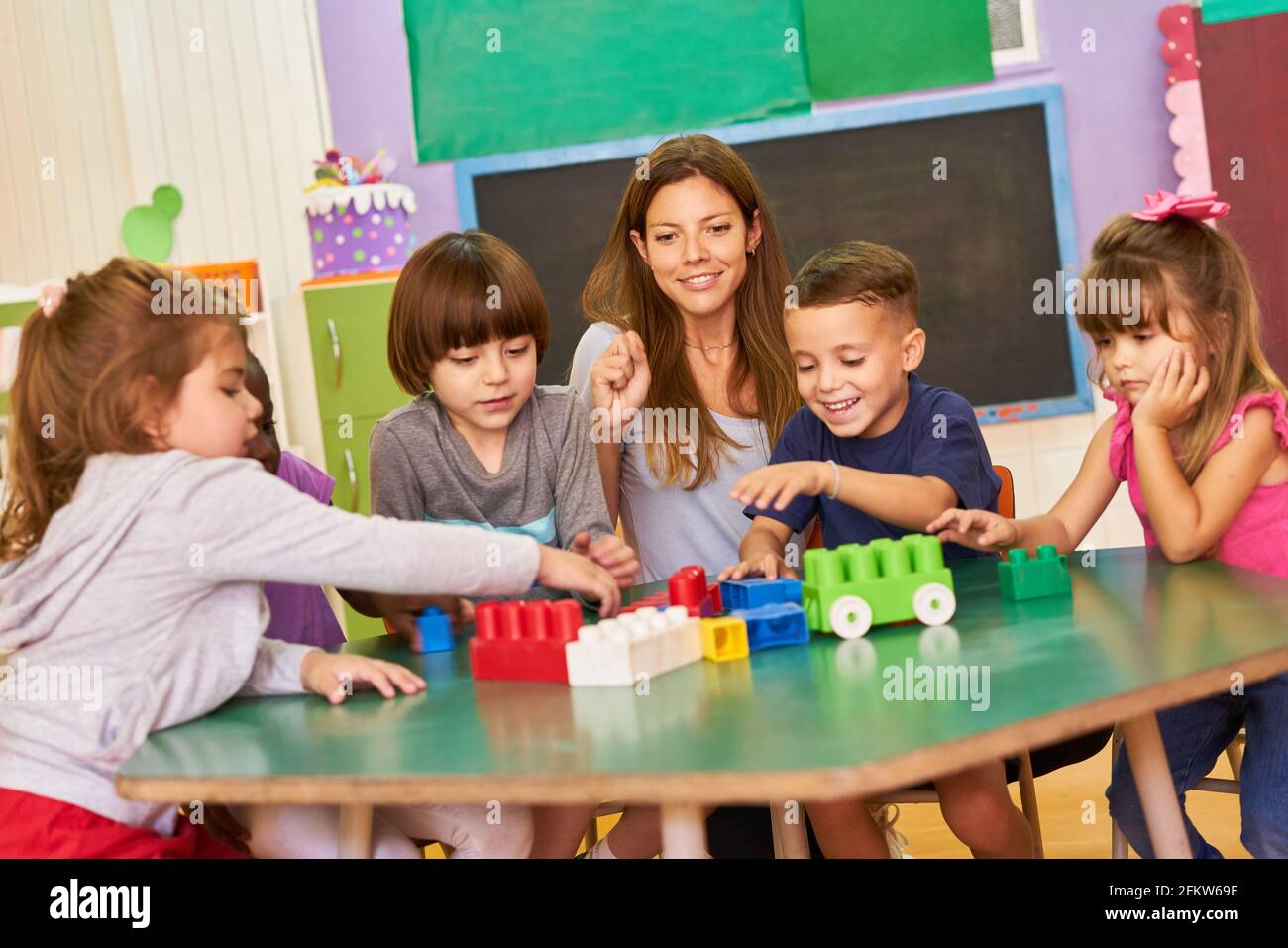 Kindergartengruppe spielt mit Bausteinen in der Kindertagesstätte Zusammen mit einer Kindergärtnerin Stockfoto