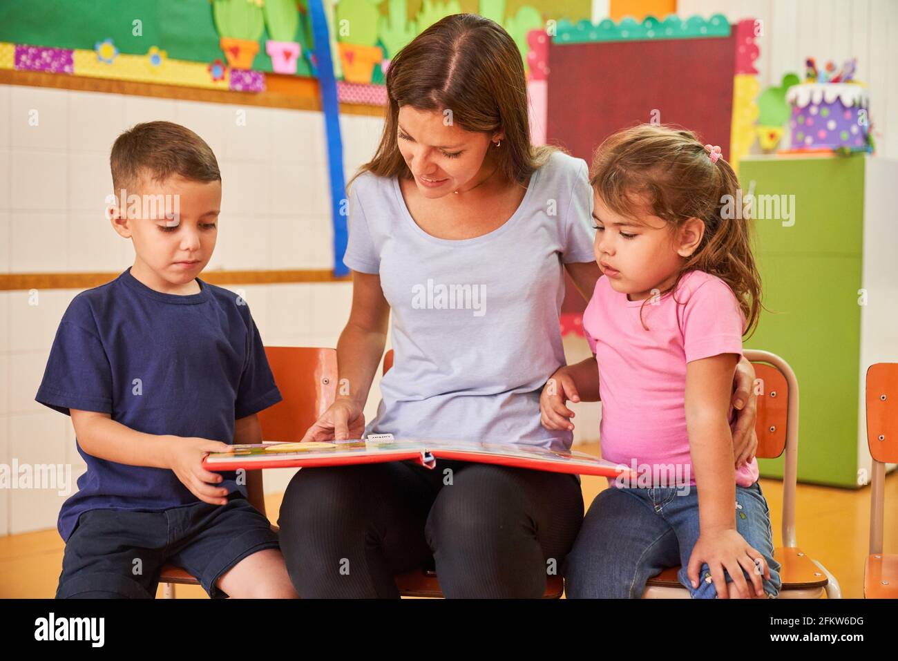 Pädagoge oder Kinderbetreterin beim Lesen eines Buches für zwei Kinder in Eine Kindertagesstätte oder Kindertagesstätte Stockfoto