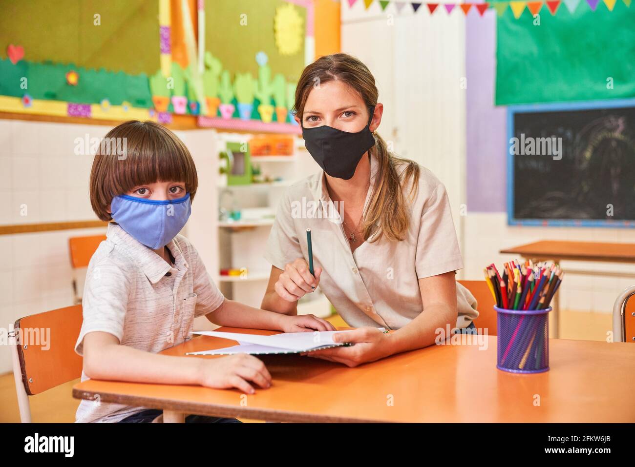 Kinderbetreung und Kind mit Gesichtsmaske wegen Covid-19 Zoll Vorschule oder Grundschule Stockfoto