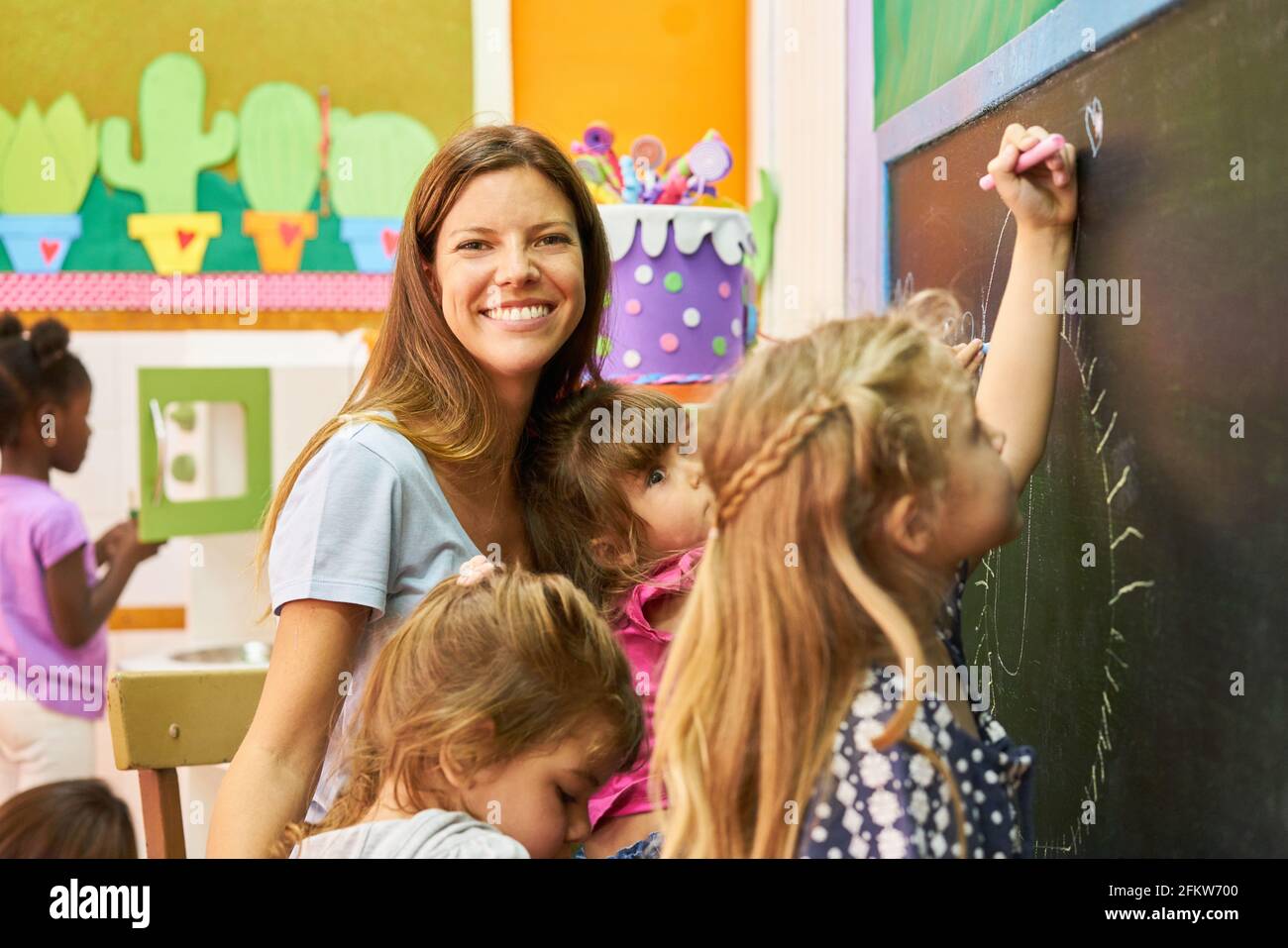 Lächelnde Erzieherin und Kinder zusammen an der Tafel im Kindergarten Oder im Vorschulalter Stockfoto