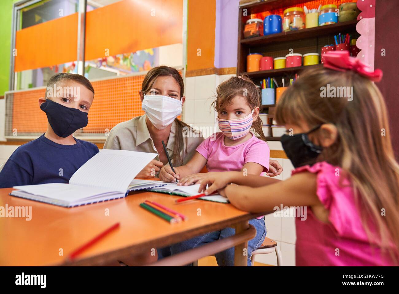 Kinder und Erzieher in einer Kindertagesstätte während des Studiums mit Gesichtsmasken wegen Covid-19 und Coronavirus Stockfoto