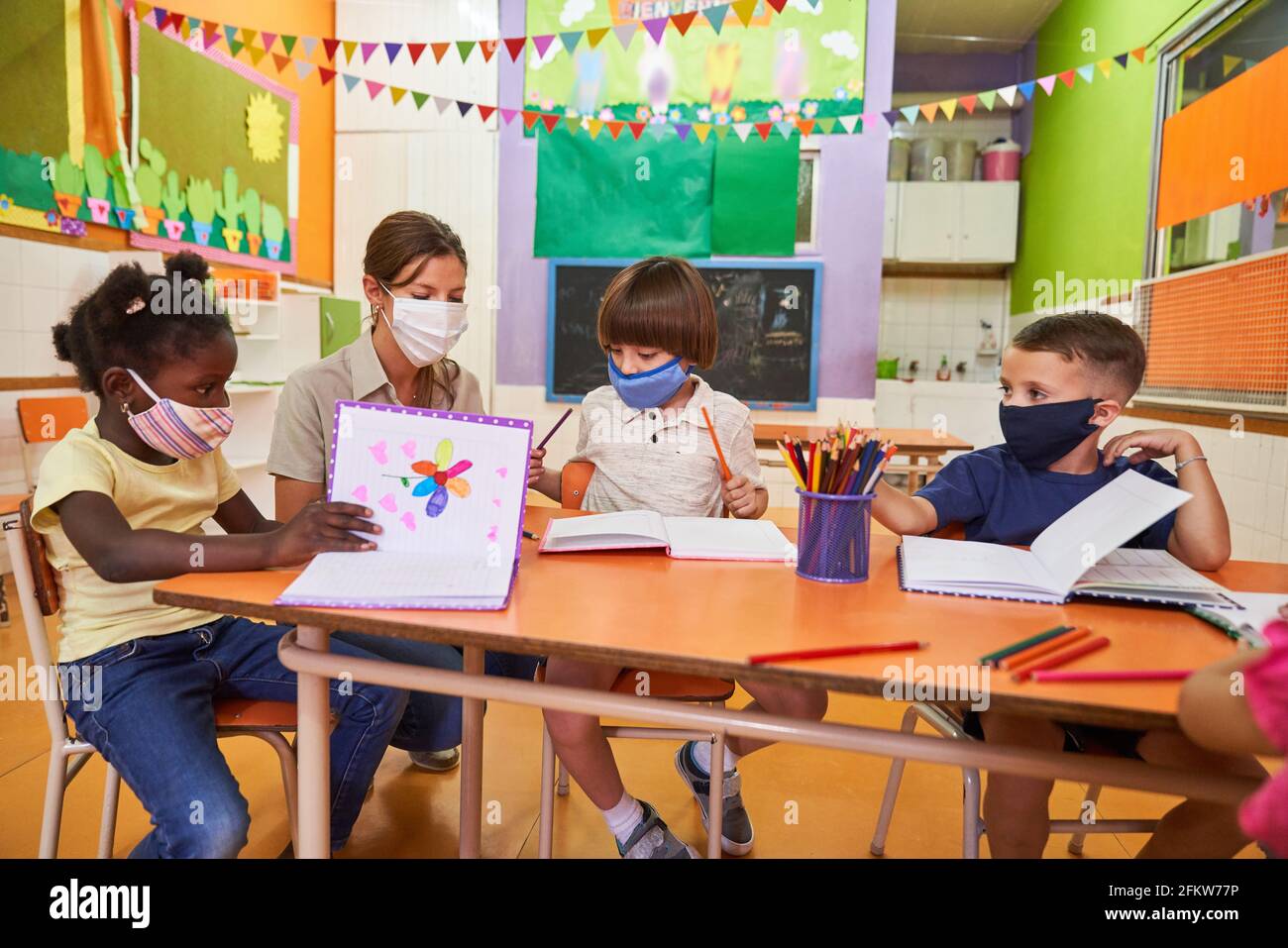 Multikulturelle Gruppe von Kindern malt mit Buntstiften am Tisch In der Kindertagesstätte mit einem Pädagogen Stockfoto