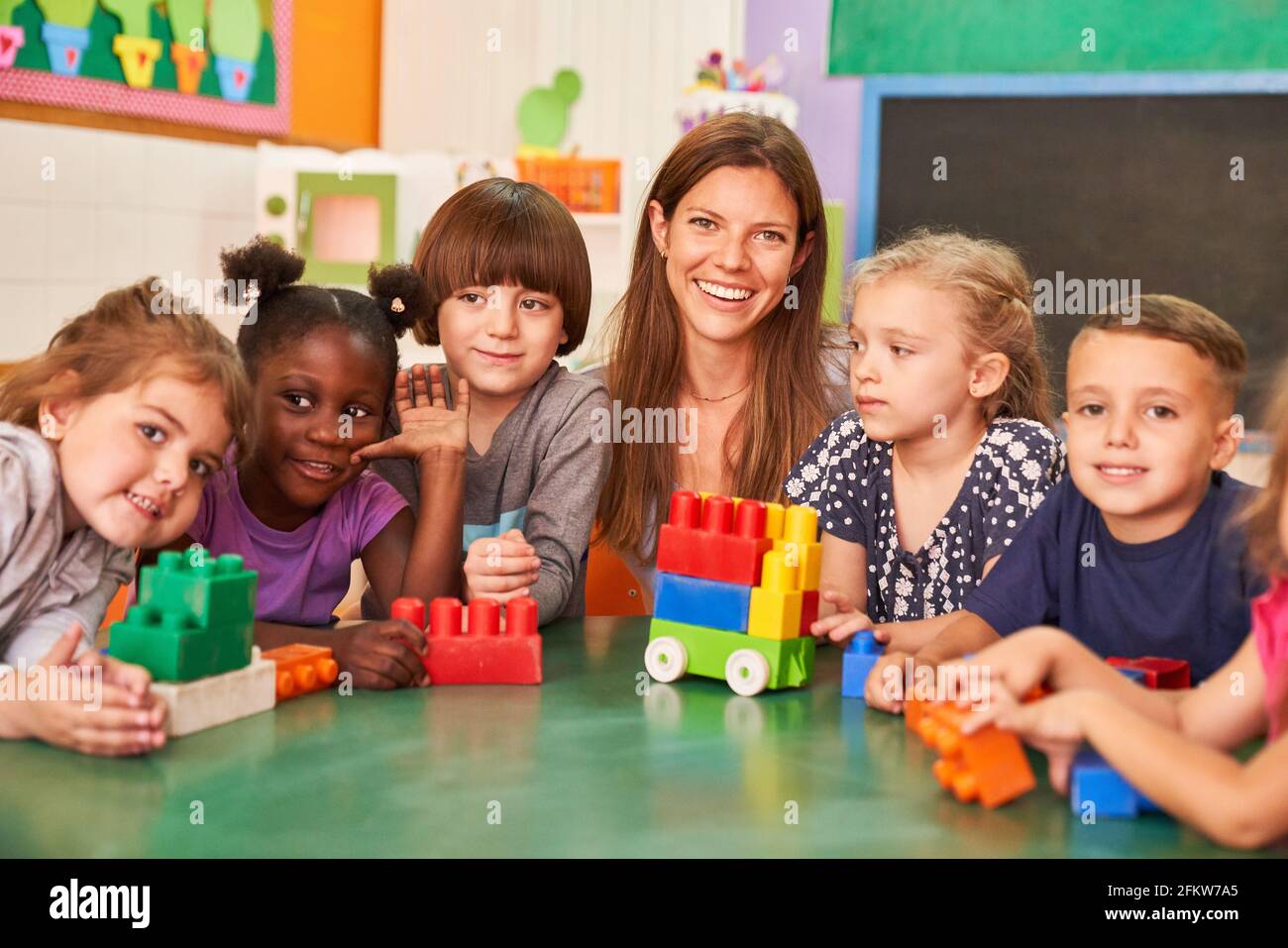 Gruppe von glücklichen Kindern im internationalen Kindergarten mit Kindergärtnerin Und Bausteine Stockfoto