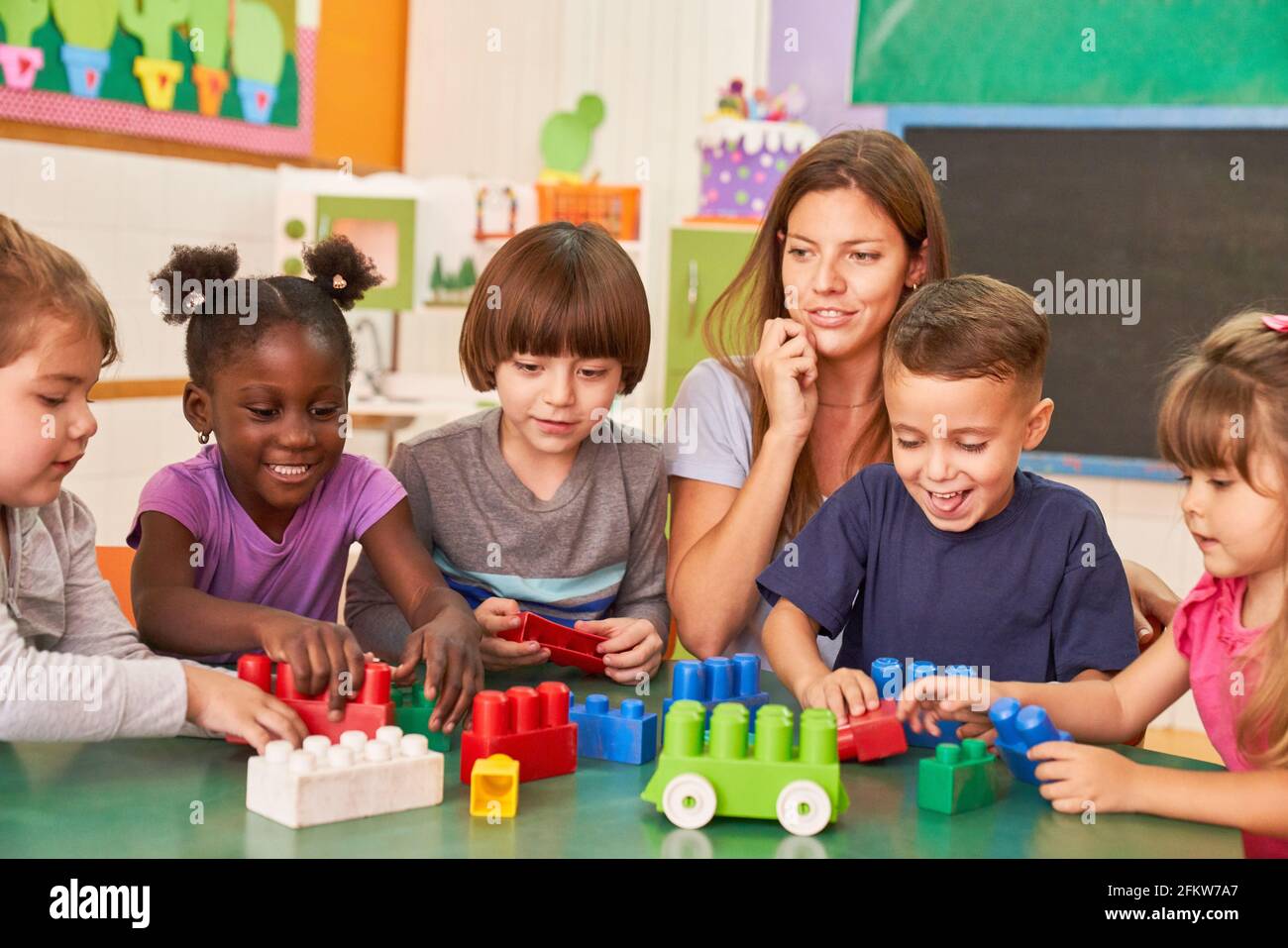 Eine Gruppe von Kindern spielt in der Kindertagesstätte mit einem Pädagogen zusammen Und Bausteine Stockfoto