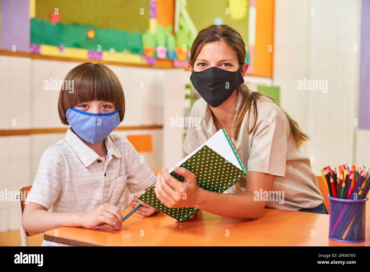 Lehrer hilft Kind mit Maske wegen Covid-19 in der Schule Mit Hausaufgaben Stockfoto