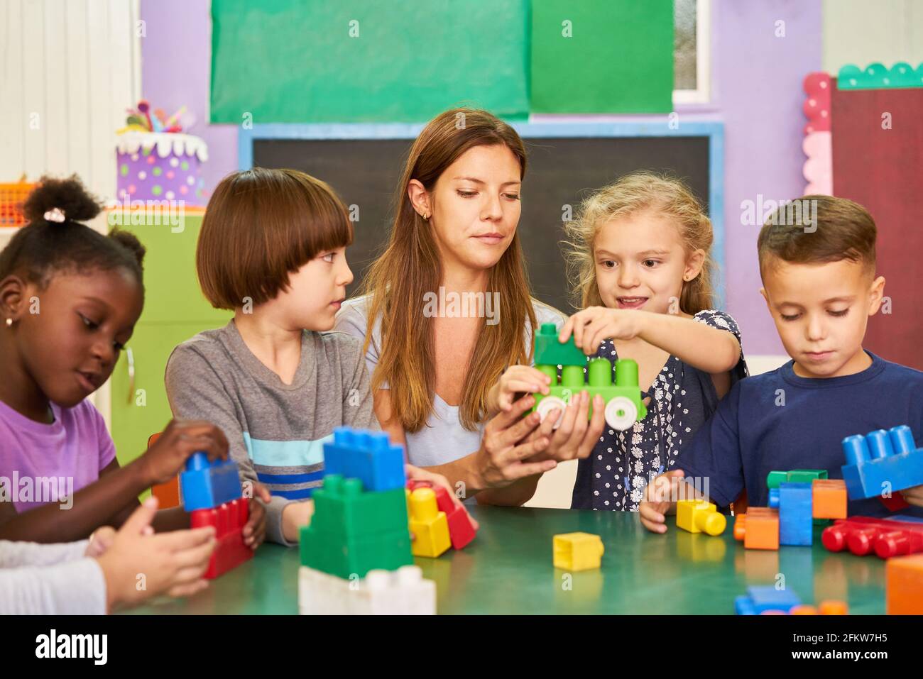 Gruppe von Kindern spielt im Kindergarten mit Kindergärtnerinnen mit Blöcke am Tisch Stockfoto