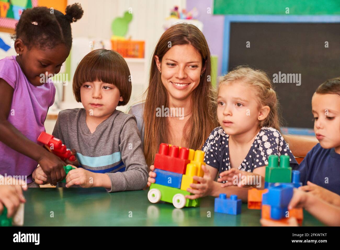 Kinder spielen zusammen mit bunten Bausteinen in der Kindertagesstätte oder Nachschulpflege mit einem Pädagogen Stockfoto