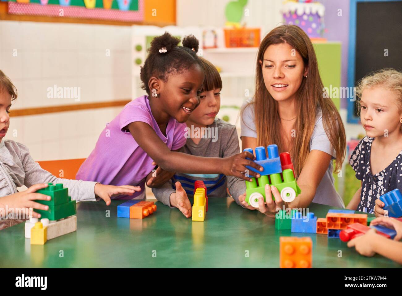 Im internationalen Kindergarten spielen Kinder mit Bausteinen zusammen Mit einer Kindergärtnerin Stockfoto