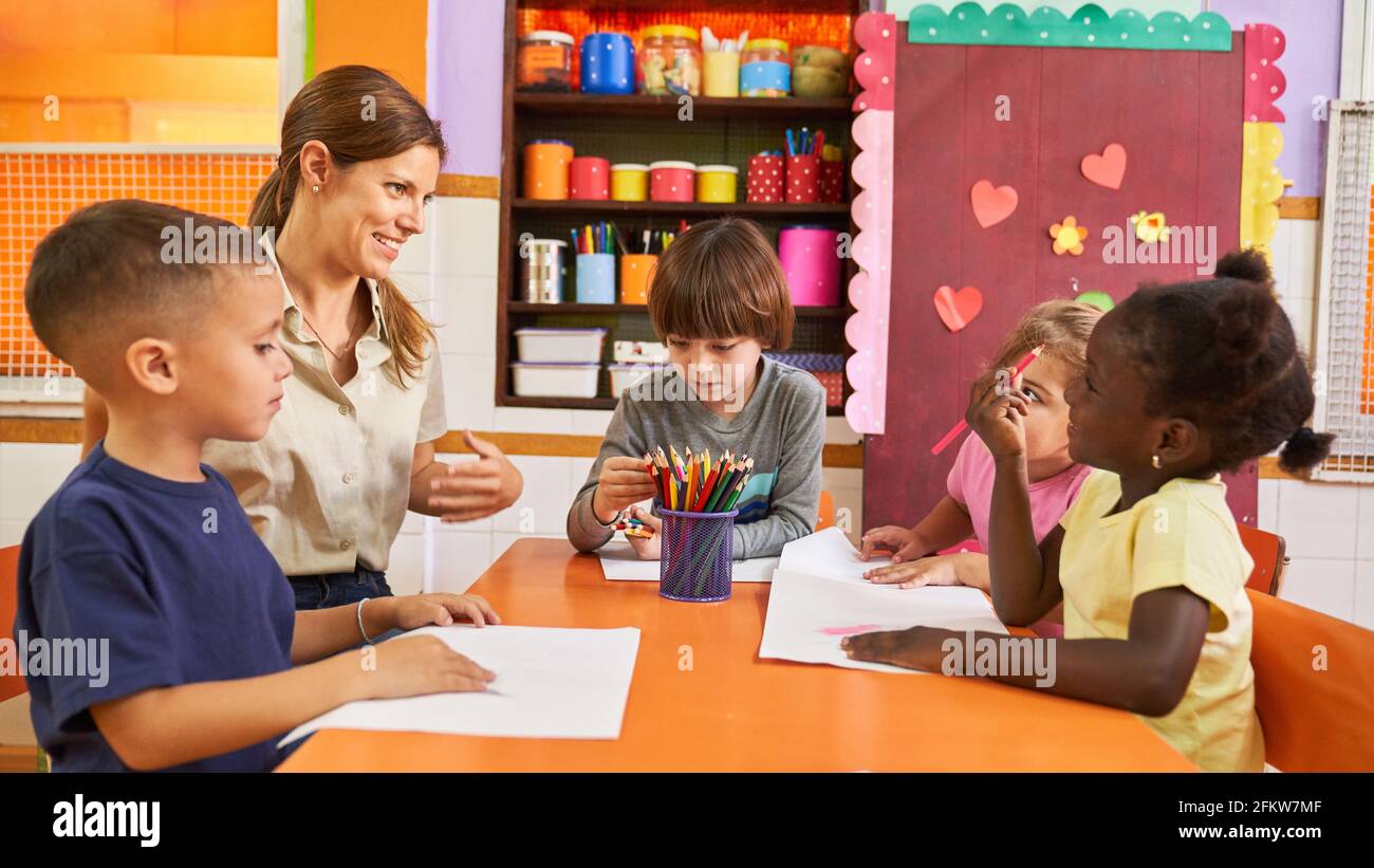 Multikulturelle Gruppe von Kindern malt mit Buntstiften in der Kindertagesstätte mit Ein Pädagoge am Tisch Stockfoto