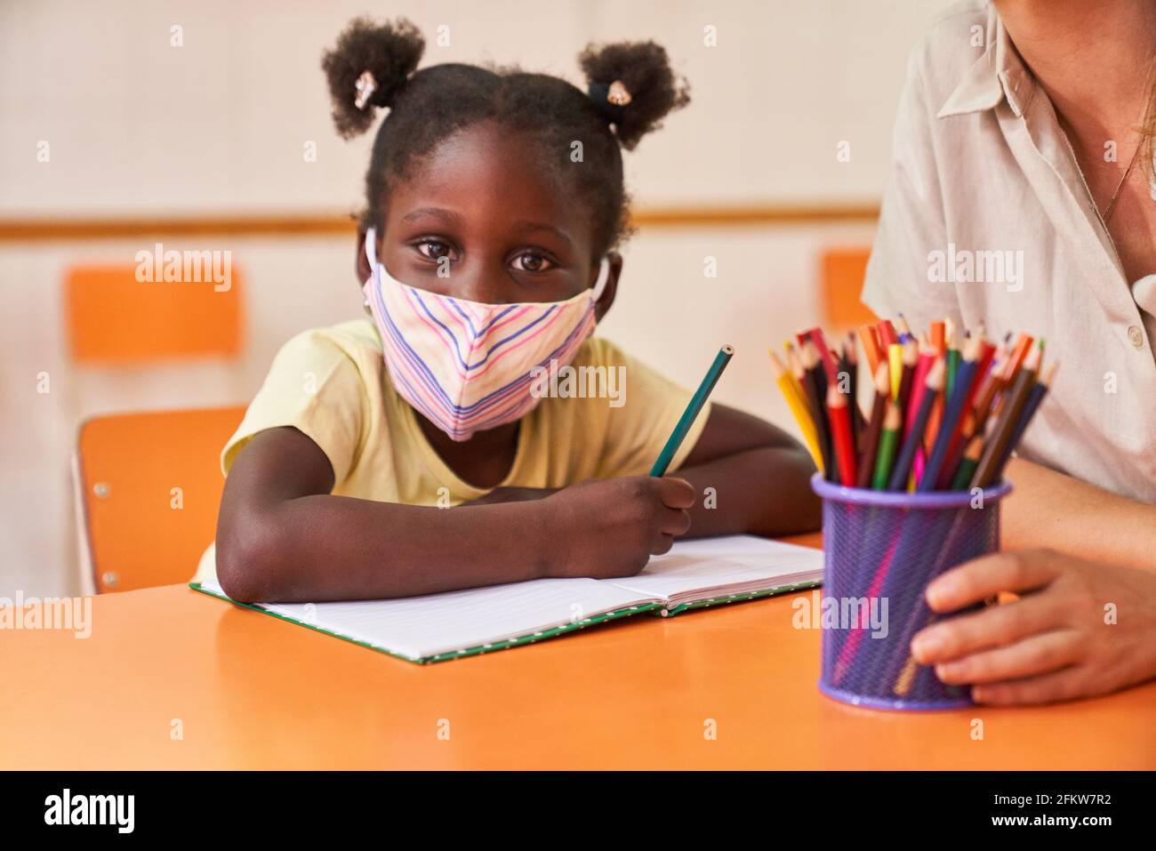 Afrikanisches Mädchen mit Gesichtsmaske wegen Covid-19 beim Malen Ein Bild in der Vorschule Stockfoto